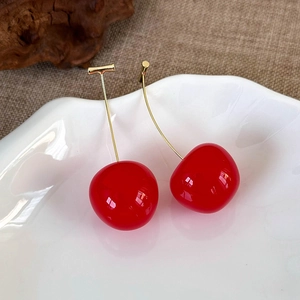 Detailed view of glossy red cherry earrings with gold metal stems on a white plate