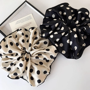 Detailed view of large polka dot satin scrunchies in cream and black on a display tray