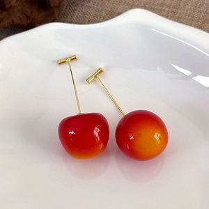 Close-up of glossy red cherry earrings on a white ceramic plate with golden stems