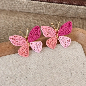 Close-up of handmade pink raffia butterfly earrings on a natural linen background