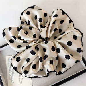 Detail of cream oversized polka dot scrunchie with black edge stitching on a display tray