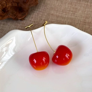 Macro detail of red resin cherry earrings with golden stems on white ceramic tray