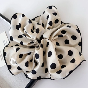 Detail of a large silk-textured beige scrunchie with bold black polka dots and fine stitching