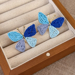 Macro detail of hand-woven butterfly earrings with raffia texture and golden metal accents