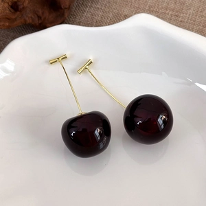 Close-up of cherry-shaped earrings with red resin charms on a white textured dish