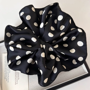Detailed close-up of large black polka dot scrunchie with silky satin texture and white patterns
