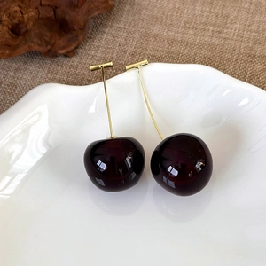 Close-up of deep burgundy cherry earrings with golden stems on a stylish white tray