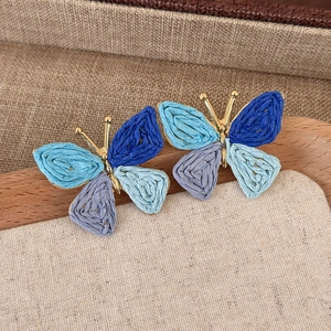 Close-up of woven raffia butterfly earrings with vibrant blue and purple wings