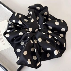 Close-up of a large black satin scrunchie with white polka dots and elegant silk texture