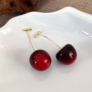 Macro detail of realistic cherry drop earrings with deep red resin and gold stems