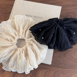 Close-up of cream and black pleated scrunchies with elegant pearl embellishments