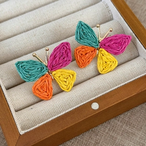 Detailed close-up of handmade colorful woven raffia butterfly earrings in a jewelry box