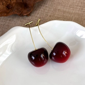 Detail showing red translucent cherry earrings with golden hooks on white porcelain