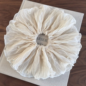 Detail of cream oversized pleated scrunchie with pearl beads on fabric texture