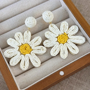 Detailed close-up of handmade woven daisy earrings with white petals and yellow center