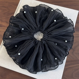 Detail of elegant black pleated scrunchie with white pearl accents on book surface