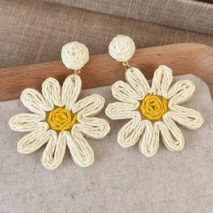 Macro shot of oversized woven straw daisy earrings with textured yellow centers