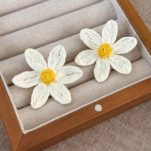 Close-up of woven raffia daisy earrings in white and yellow on a wooden jewelry display