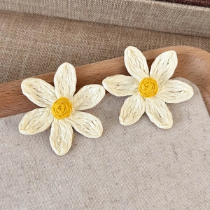 Macro detail of handmade woven daisy earrings with white raffia petals and yellow centers