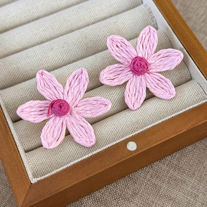 Macro detail of handmade pink woven flower earrings with delicate fiber texture