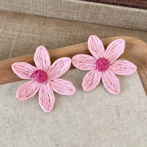 Macro shot of pink woven straw floral earrings on a rustic tray showing handmade texture