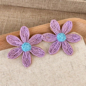 Macro view of purple hand-woven straw flower earrings with a blue core on burlap