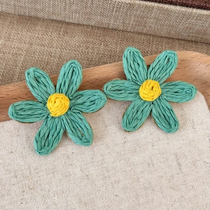 Detailed macro view of handmade woven raffia flower earrings in vibrant teal and yellow