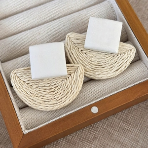 Detail of bohemian straw woven earrings with white resin square top on linen background