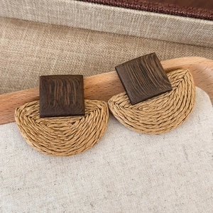 Detail of bohemian geometric woven straw and dark wood square stud earring on a rustic tray
