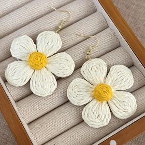 Close-up of handmade woven straw daisy earrings with yellow centers on a jewelry box