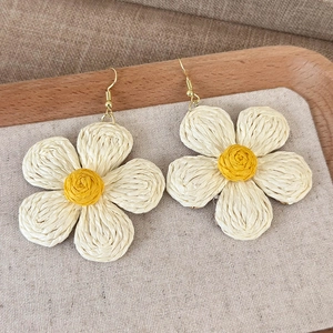 Detailed view of handmade woven straw flower earrings with yellow center and gold hooks