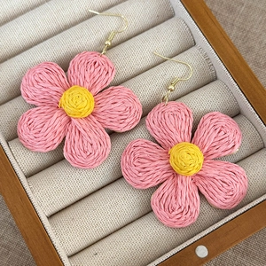 Detail of pink and yellow woven straw flower earrings with golden hooks in a jewelry box