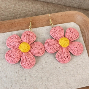 Detail of hand-woven pink raffia flower earrings with yellow centers and gold metal hooks