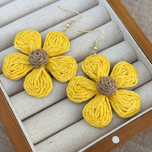 Macro detail of sunflower woven earrings with yellow straw petals in a jewelry box