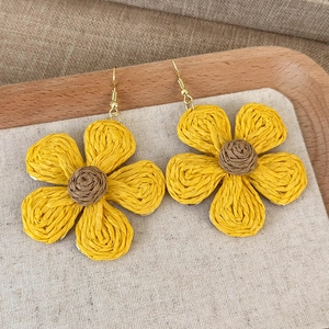 Macro detail of sunflower raffia earrings with yellow woven petals and golden hooks