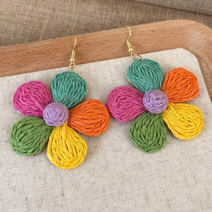Close-up of colorful raffia woven flower earrings with golden hooks on wooden tray
