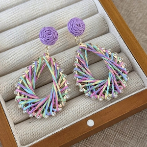 Detailed macro shot of bohemian rainbow woven teardrop earrings with purple rose stud