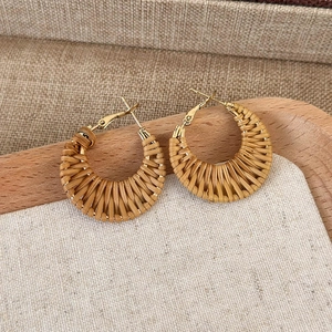 Macro detail of natural straw woven hoop earrings with gold metal fasteners on wood
