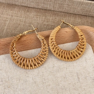 Macro shot of bohemian woven straw hoop earrings with golden metal studs on linen background