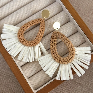 Detail of bohemian drop earrings with brown woven rattan and white raffia tassels