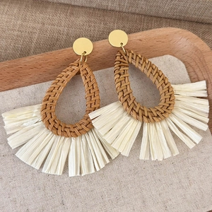 Close-up of Bohemian woven rattan drop earrings with straw tassels on a rustic wood background