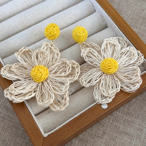 Detailed macro view of woven cream sunflower earrings with yellow core on wood display