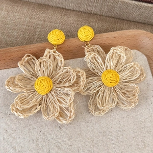 Close-up of woven straw sunflower earrings with beige petals on a natural linen fabric