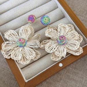 Close-up of handmade woven floral earrings with raffia texture and colorful spiral core