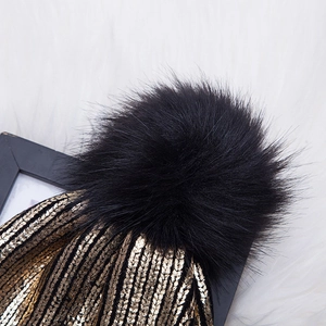 Close-up of winter knit beanie with black faux fur pompom and gold metallic stripes