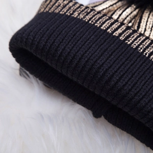 Close-up of black knit beanie with gold foil vertical stripes and faux fur pompom