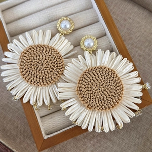 Detail of sunflower earrings with woven raffia centers and white fabric petals in jewelry box