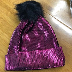Detail of rose red metallic knit hat with a large black faux fur pom pom on top
