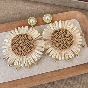 Detail of woven flower earring with pearls and rhinestones on rustic background