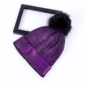 Close-up of purple knit beanie with metallic glitter yarn and black faux fur pompom